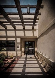 Sunlight casts geometric shadows from a wooden pergola onto a walkway and building facade.