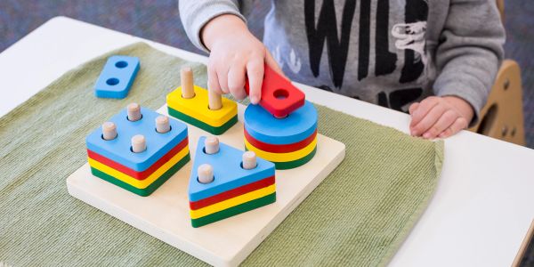 Child playing with colorful shape sorting toy on a table.
