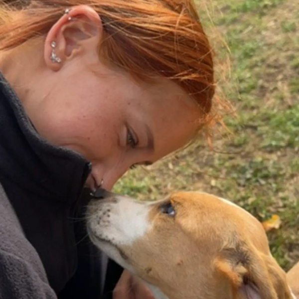 A woman and a dog share a tender nose-to-nose moment outdoors.