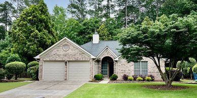 A well-maintained brick house with a manicured lawn and large tree in front.