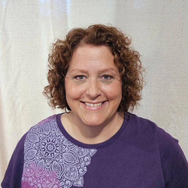 Smiling woman with curly hair wearing a purple shirt with a decorative pattern.