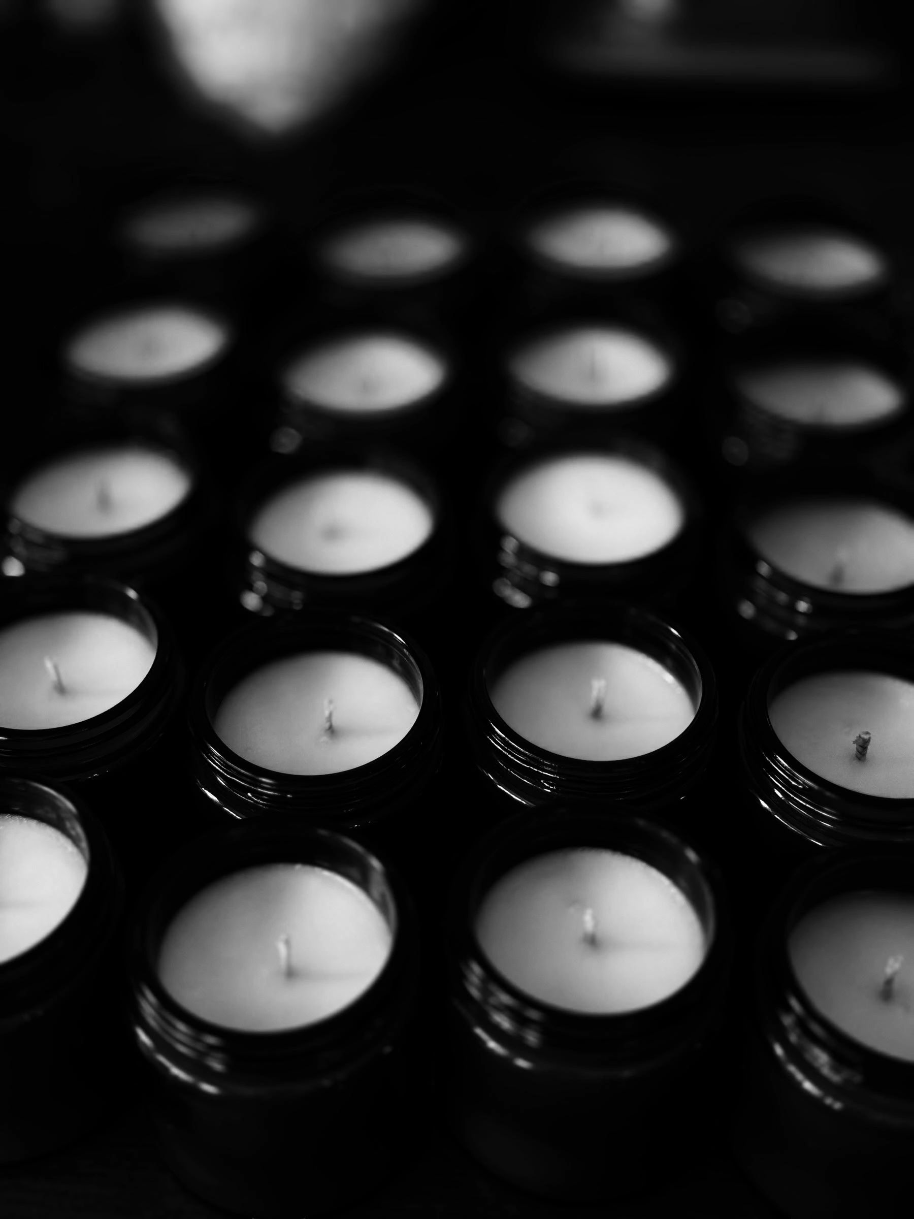 Rows of unlit candles in black jars arranged neatly.