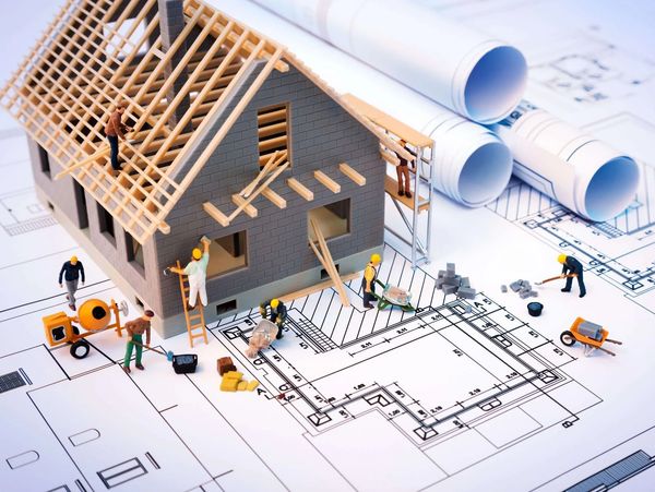 Miniature construction workers building a house model on architectural blueprints.