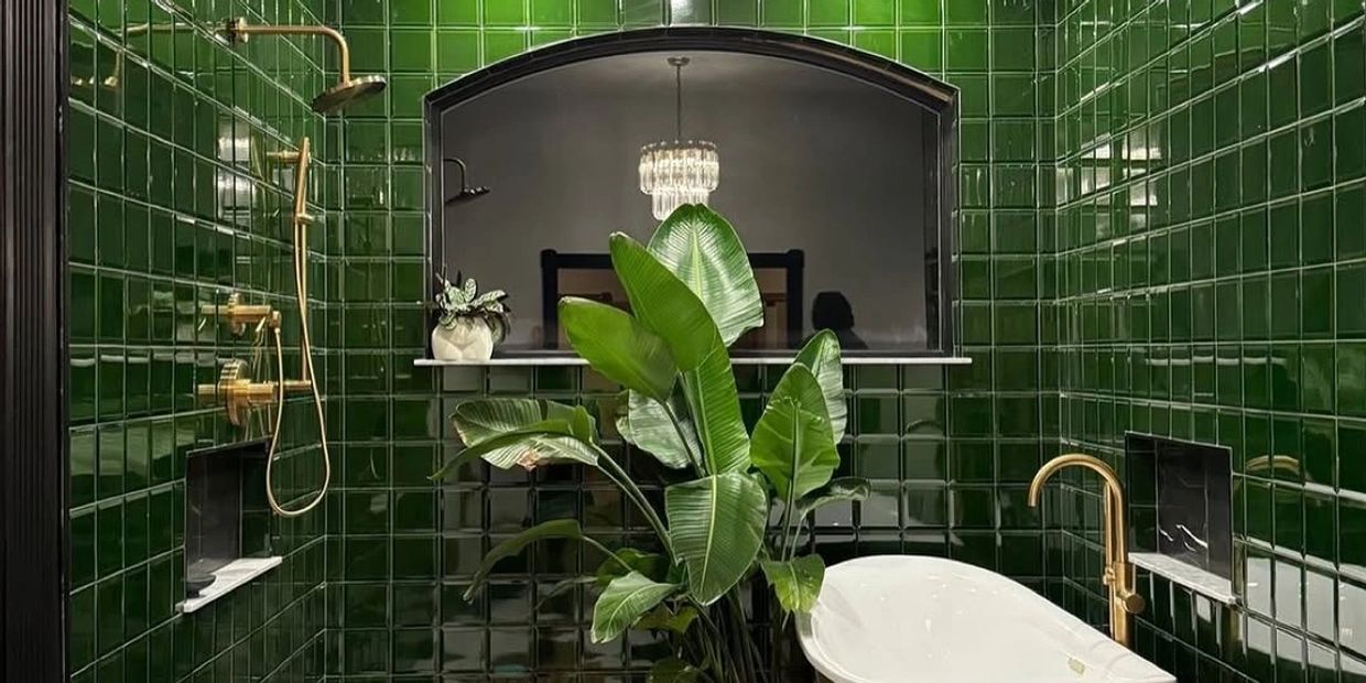 Luxurious bathroom with glossy green tiles, gold fixtures, and a large leafy plant.