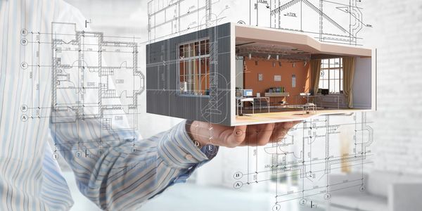 Hand holding a 3D architectural model with building plans in the background.