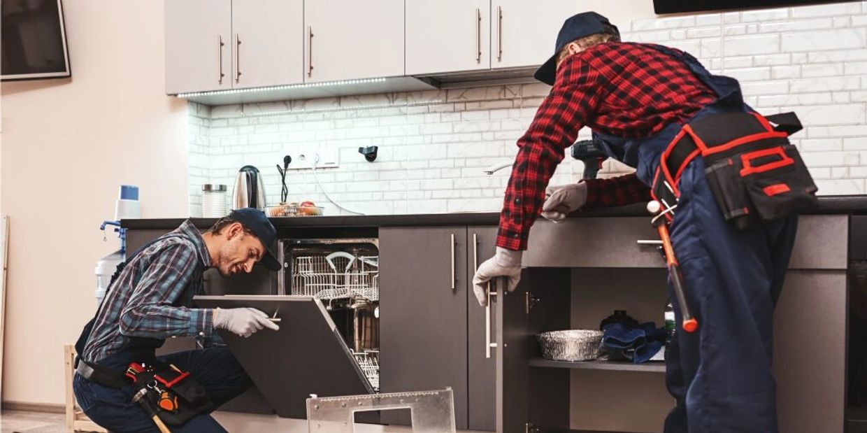Two technicians repairing a dishwasher in a modern kitchen.