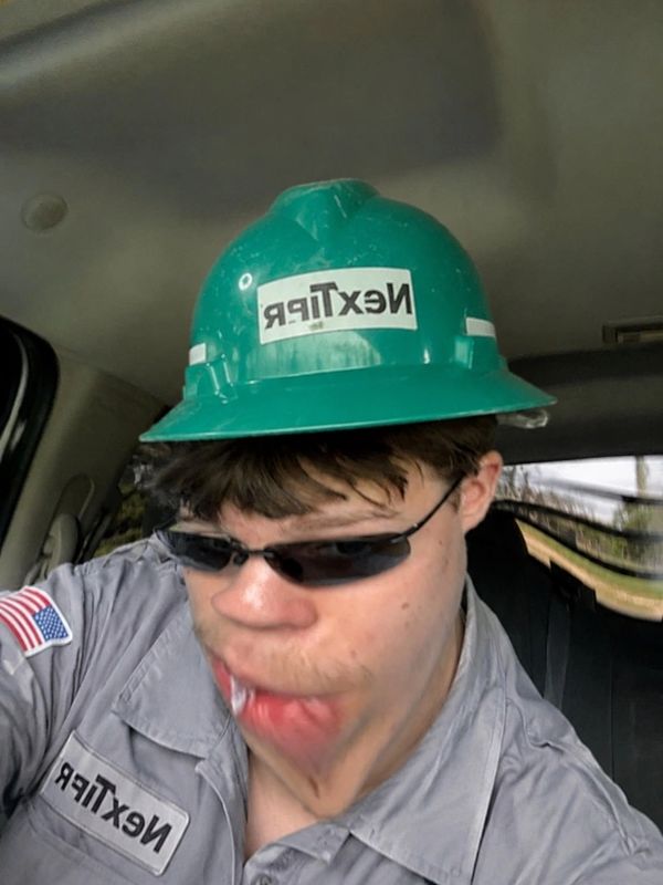 Man in work uniform and green hardhat with distorted face inside a vehicle.