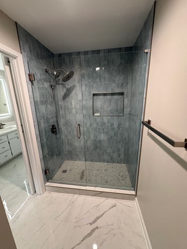Modern walk-in shower with blue tiles and glass door.