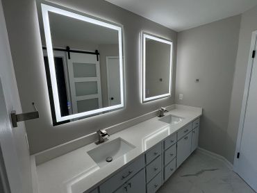 Modern bathroom with double sinks and illuminated mirrors.