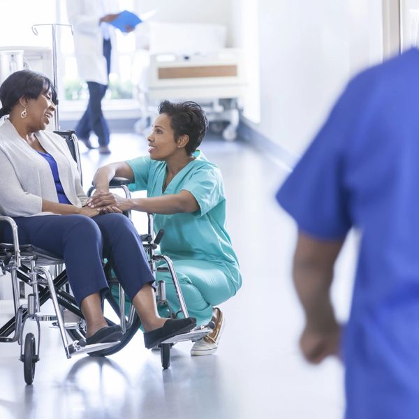 Nurse comforting a woman in a wheelchair in a hospital hallway.