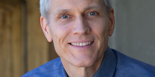 Smiling real estate broker with blue eyes and gray hair in a blue shirt.