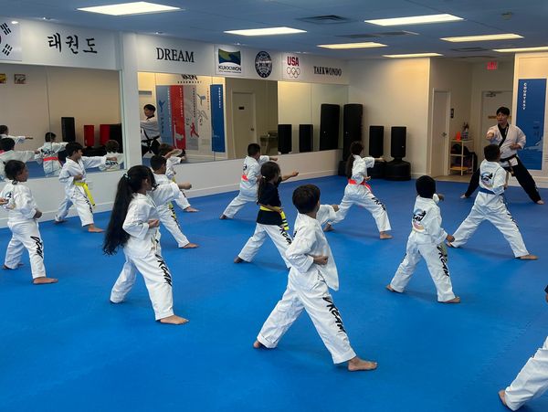 Children practicing taekwondo in a bright, spacious studio with instructor.