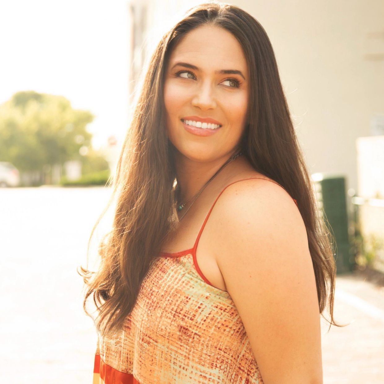 Smiling woman with long hair outdoors in sunlight.
