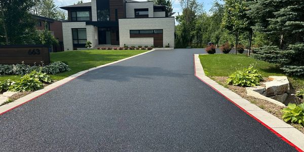 Smooth black driveway leading to a modern house with a well-kept lawn.