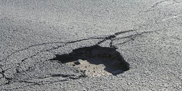 A pothole on a cracked asphalt road surface.