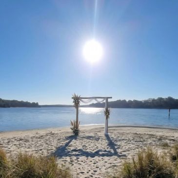 Sunlit wedding arch on a sandy beach by the water.