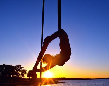 Aerialist silhouette performing at sunset by the water.