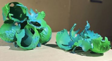 Broken green plastic objects with intricate holes and textures on a flat surface.