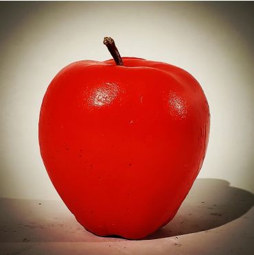 A shiny red apple with a small stem casting a shadow.