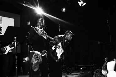 Two musicians perform energetically on stage in a black-and-white photo.