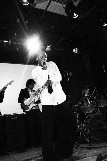 Black and white photo of a band performing live on stage with a singer in front.