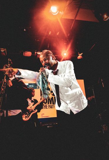 Energetic singer with microphone and band performing on stage under warm lights.