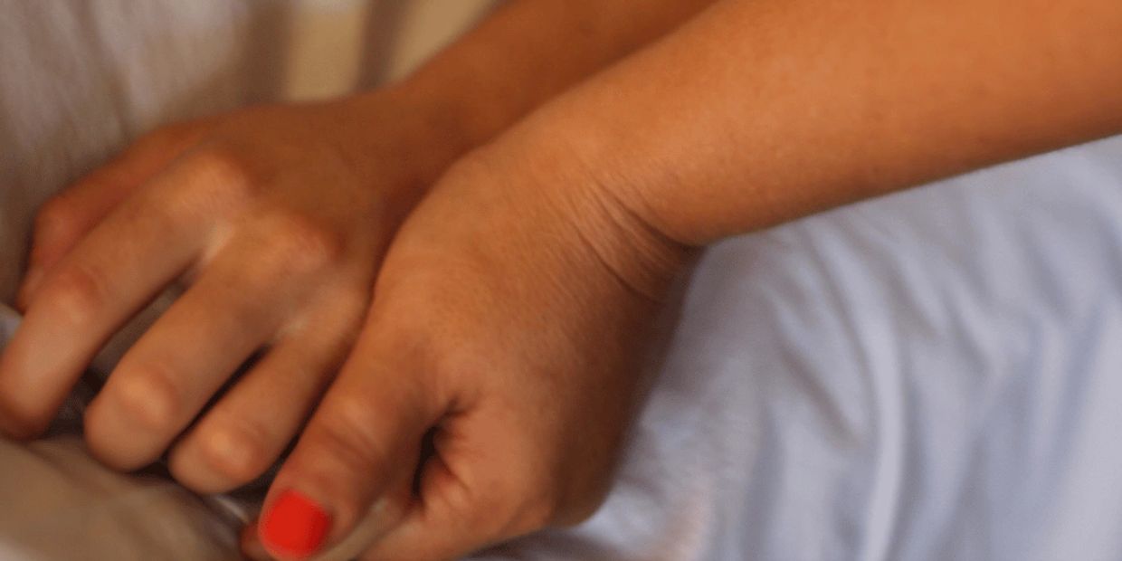 Close-up of two hands intertwined, one with red nail polish.