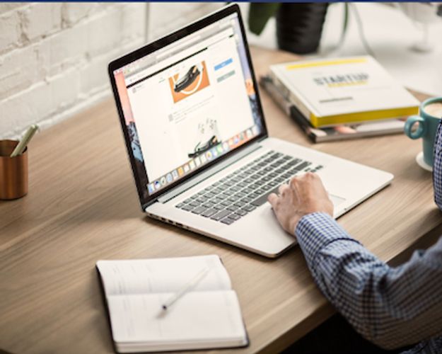 Person browsing shoes on a laptop while working at a desk.