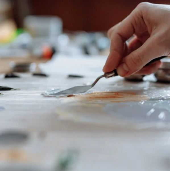 Hand using a palette knife to mix paint on a surface.