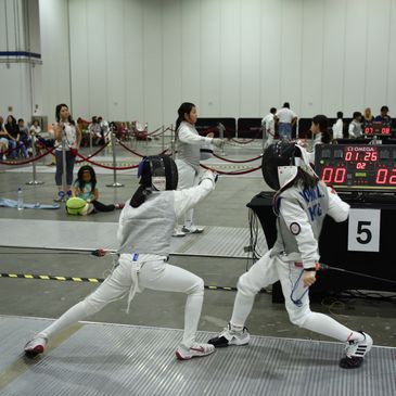 Two fencers engaged in a competitive bout in an indoor arena.
