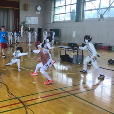 Children practicing fencing in a gymnasium with coaches and equipment.