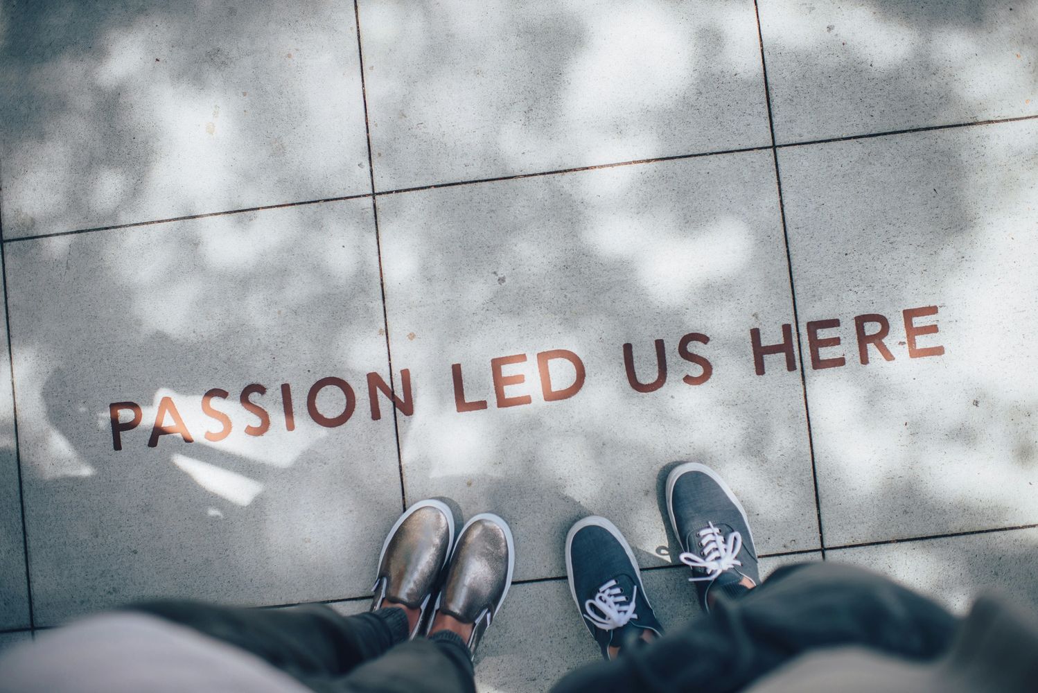 Image of two feet next to the wording "PASSION LED US HERE" on a side walk.