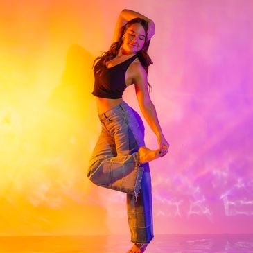 Woman striking a joyful dance pose against vibrant yellow and purple lighting.