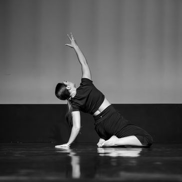 A woman in black performs a graceful dance pose on a reflective floor.