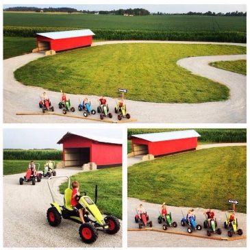 Children riding pedal go-karts on a track near a red shed.