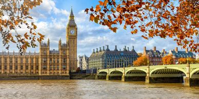 Big Ben and Westminster Bridge in autumn, framed by colorful leaves.