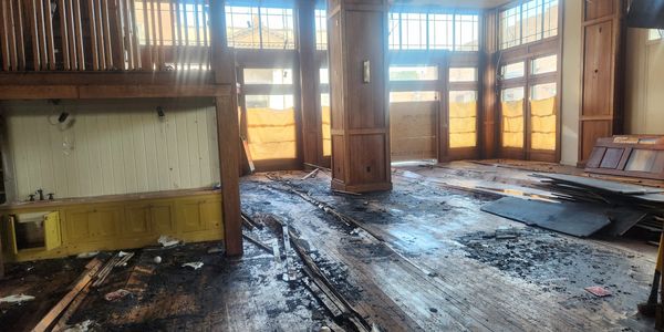 Interior of a fire-damaged room with debris and soot on wooden floors.
