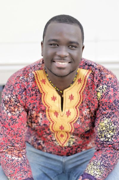 Smiling man in colorful traditional African shirt sitting relaxed.