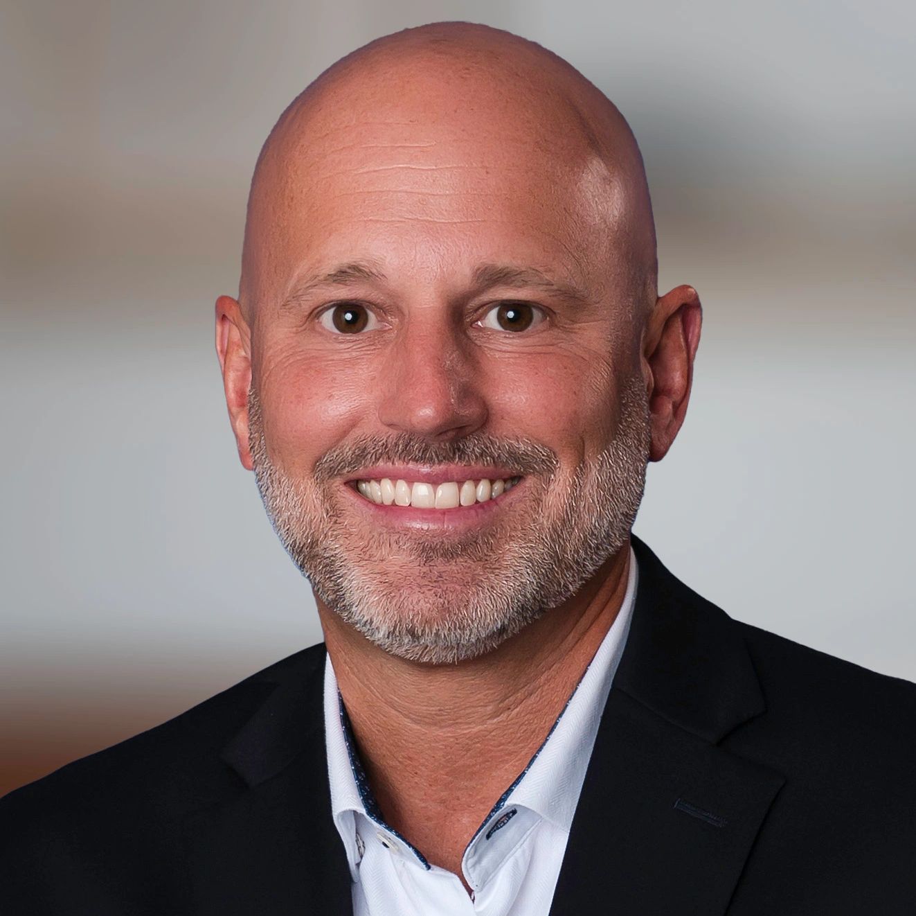 Smiling bald man with a beard in a suit jacket and white shirt.
