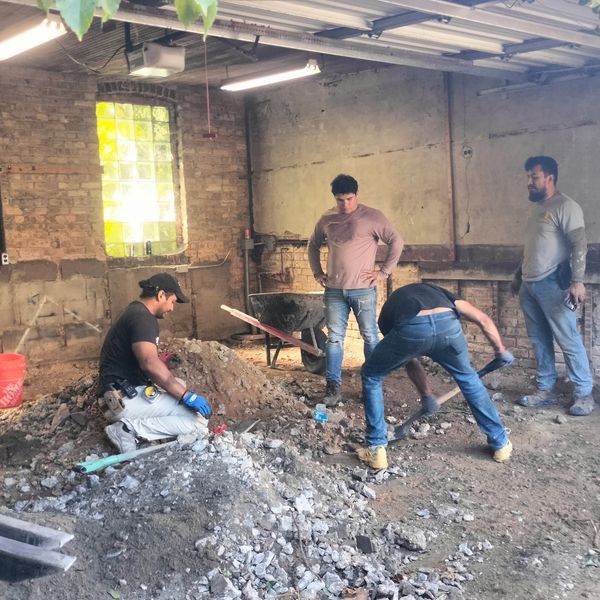 Four men working on construction or renovation in a rustic indoor space with exposed brick walls.
