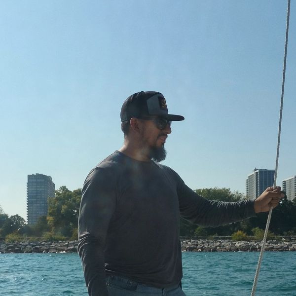 Man in a cap holding a rope on a boat under a clear sky.