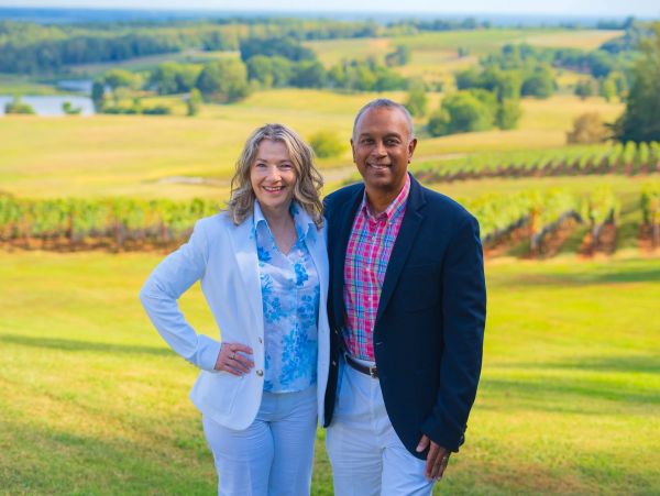 Two people standing in a sunny vineyard landscape.