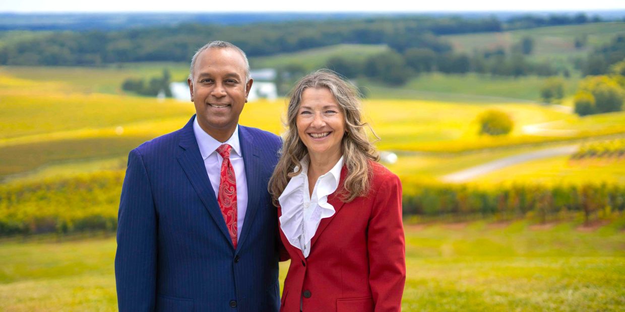 Smiling couple in formal attire standing outdoors in a scenic landscape.