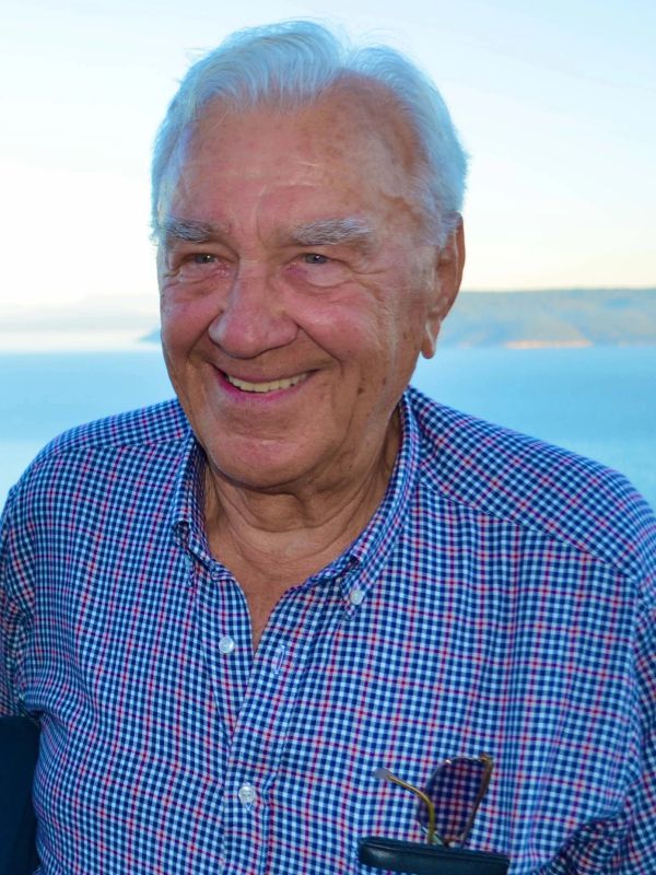 Smiling elderly man outdoors with ocean backdrop.
