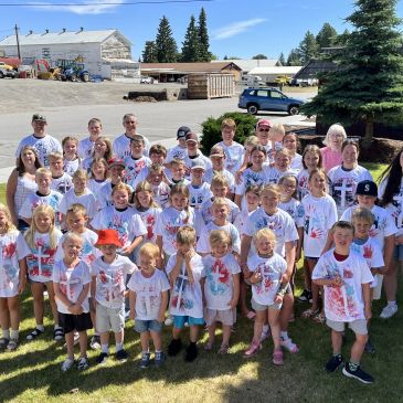 Group of kids and adults in white shirts outdoors.