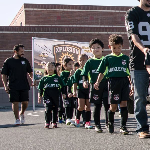 Young soccer players in green uniforms walking with their coaches outdoors.