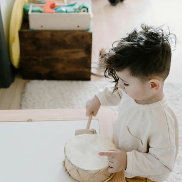 A toddler playing a small drum advertising ear and rhythm training for kids under 5 yrs.