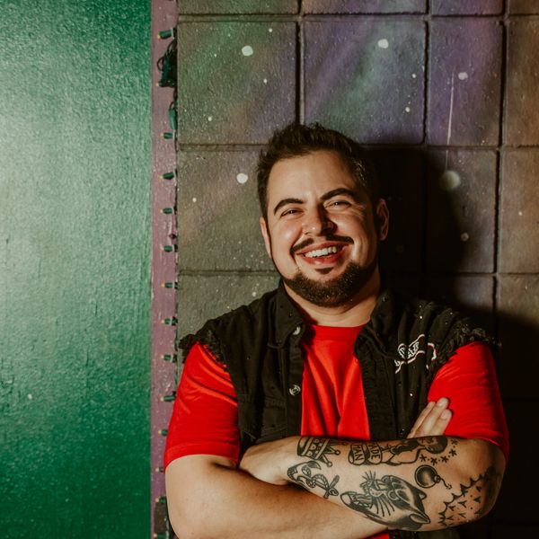 Smiling man with tattoos wearing a red shirt and black vest.