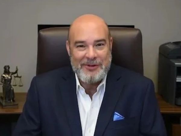 Man in a suit sitting in an office with legal decor behind him.