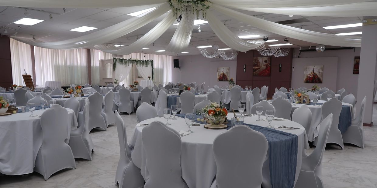 Elegant banquet hall with white drapes and floral centerpieces on round tables.